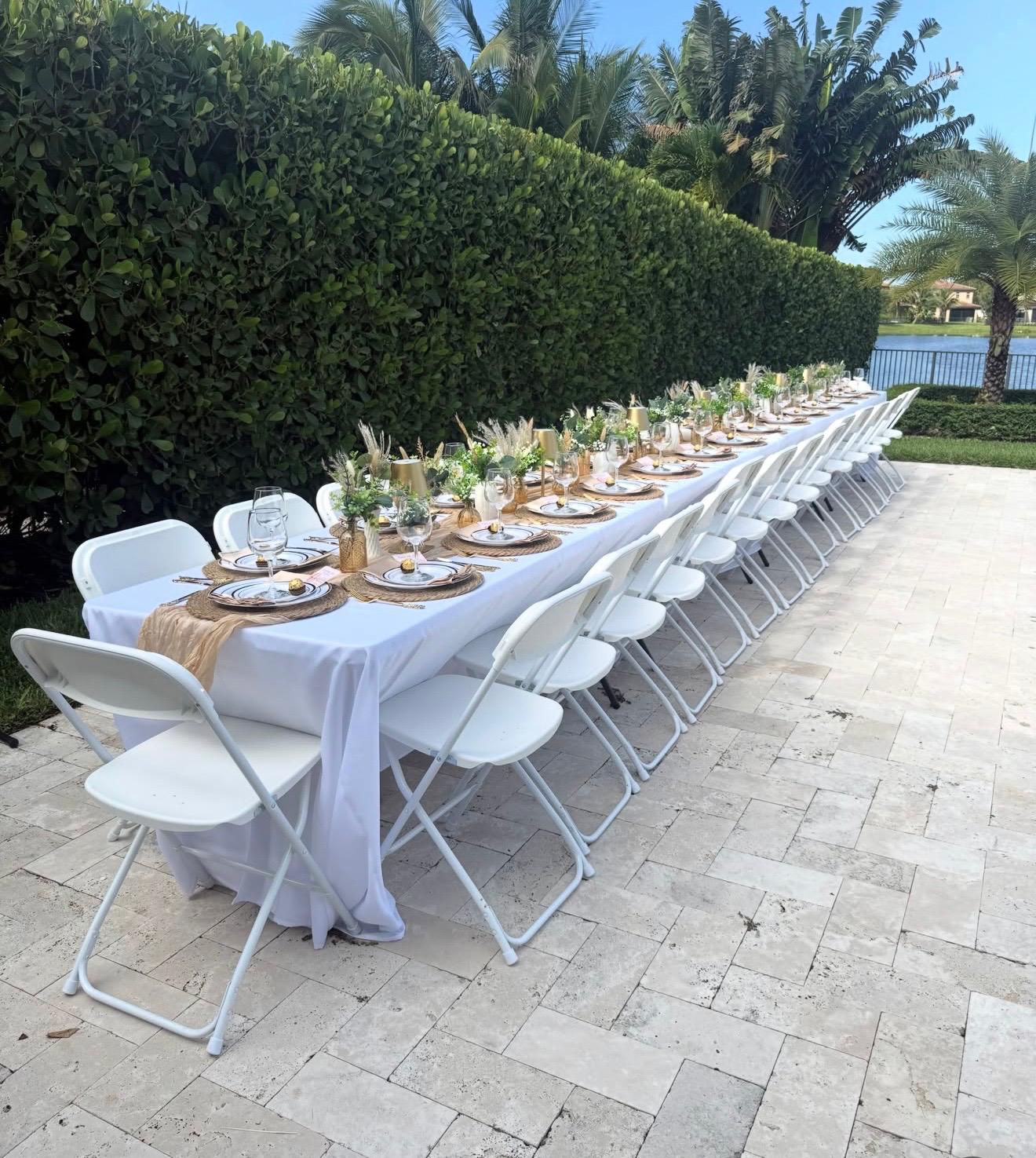 Outdoor event table setup with white chairs and elegant decor